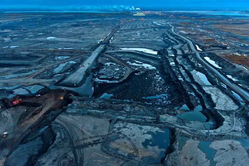 Syncrude's Mildred Lake Tar Mine in the Alberta Tar Sands Northern Alberta, Canada.

This image shows a section of Syncrude's Mildred Lake tar mine just as the sun sets. The trucks in the foreground are 400 ton capacity dump trucks so large that within its dimensions - 25'x32'x47' - a two storey 3000 sq.ft. home could be contained and provides some sense of the scale of this massive Suncor tar mine . In the background can be seen several tailings ponds, the Athabasca River, massive sulphur piles - a waste by-product of tar sands production -  and an upgrader or kind of first stage refinery -  as the tar sands are so full of impurities and of such a low grade that they require an initial level of refining before a standard oil refinery can accept them.

Twenty four hours a day the Tar Sands eats into the most carbon rich forest ecosystem on the planet. Storing almost twice as much carbon per hectare as tropical rainforests, the boreal forest is the planet’s greatest terrestrial carbon storehouse. To the industry, these diverse and ecologically significant forests and wetlands are referred to as overburden, the forest to be stripped and the wetlands dredged and replaced by mines and tailings ponds so vast they can be seen from outer space.

As of December 2016 - the latest date for which figures are available - the massive open pit mines and tailings ponds had already devastated an area of over 600 square miles or about the size of the entire city of greater London.  

The proposed full exploitation of their estimated 165 billion barrels of oil would industrialize an area the size of Florida and NASA climatologist Dr. James Hansen has noted that the associated GHG emissions would mean "game over for stabilizing the global climate."