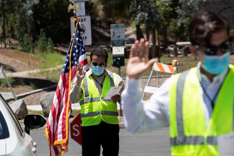 Immigration Service Officer Bay, left, leads an oath in front of Immigration Service Officer Coronel, right, during a drive-in citizenship ceremony in El Cajon, California. AP Photo