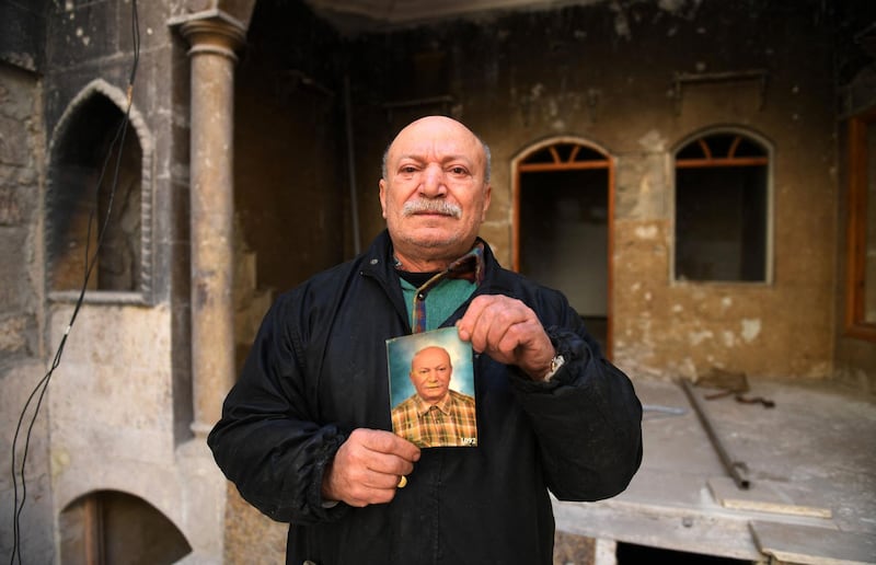 Ahmed Nashawi, also known as Abu Abdo, poses with a portrait of himself from ten prior ago outside his destroyed house in Syria's northern city of Aleppo on February 22, 2021. The man in his fifties, once one of the city's most popular fishmongers, said his home and shop on Sahat Al Hatab square were obliterated in clashes between rebels and pro-government fighters in 2015. AFP