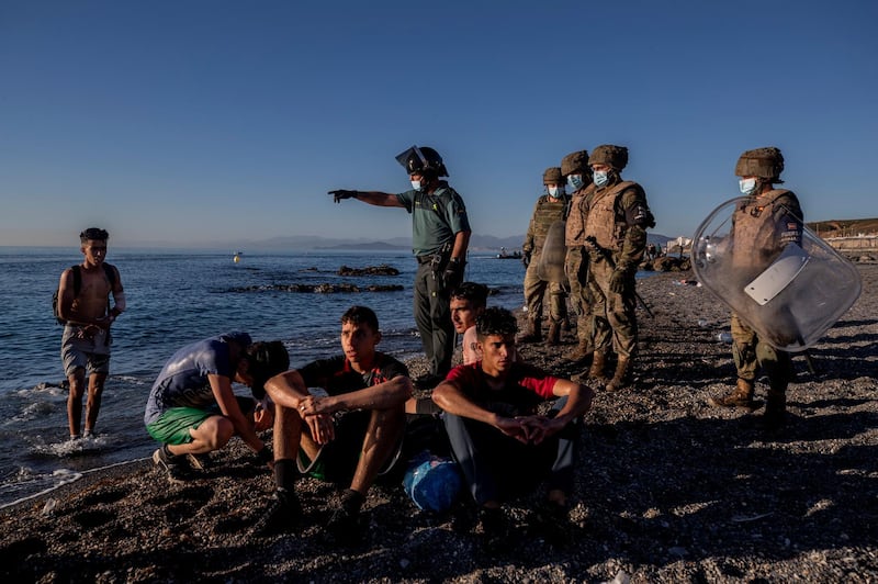 Surrounded by Spanish security forces, migrants sit on the beach after arriving at Ceuta. AP Photo