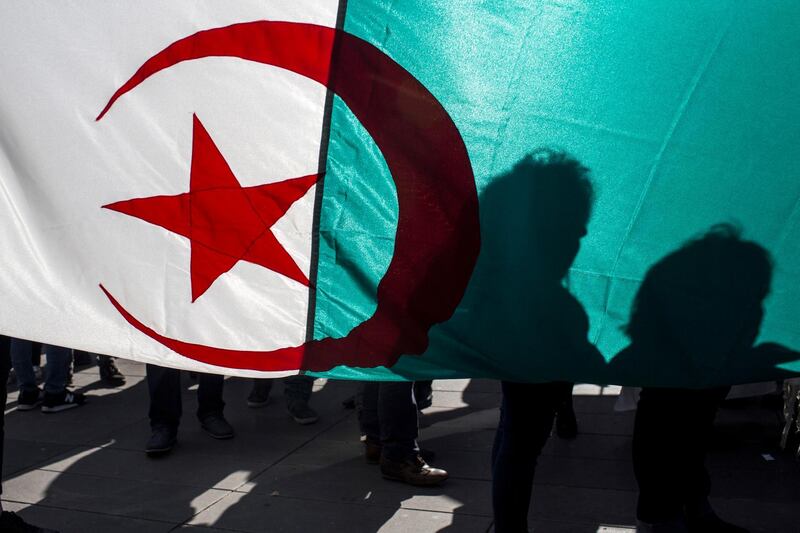 Demonstrators are silhouetted against a national Algerian flag as they stage a protest on the Republique Plaza to press for an end to the 20-year-rule of Algerian President Abdelaziz Bouteflika, in Paris, France, Sunday, March 17, 2019. (AP Photo/Rafael Yaghobzadeh)