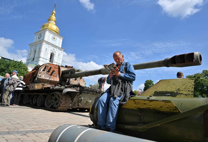 A man reads a book as he sits on a fragment of a rocket at an exhibition in Kyiv featuring Russian equipment that was damaged or destroyed during the conflict.  AFP