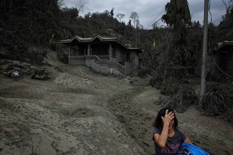 Andalida Cabono stands before her home covered in ash from the eruption of the Taal volcano, as she prepares to leave for an evacuation centre on January 17. AFP