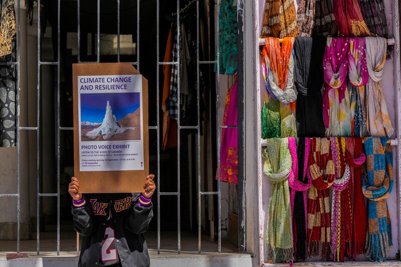 A climate activist holds a placard to advertise a local photo exhibition on climate change in Leh town.