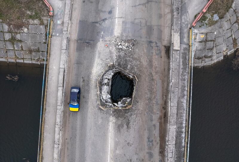 A vehicle draped with a Ukrainian flag passes over a war-damaged bridge in Makarov. Getty Images