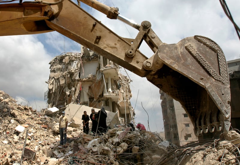 Residents watch an excavator remove rubble from damaged apartment blocks in a south Beirut suburb, September 1, 2006