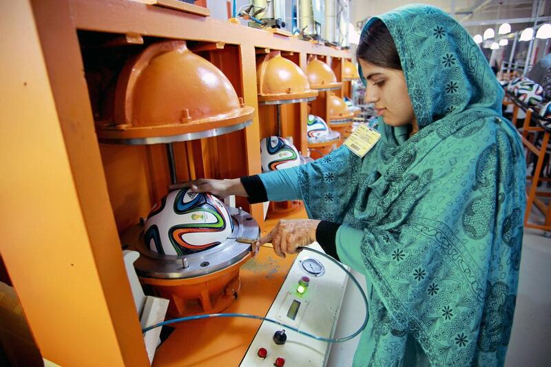 An employee holds a hose inserted into the valve of an Adidas AG "Brazuca" football in a thermo-bonding molding machine on the production line at the Forward Sports Ltd factory in Sialkot, Punjab. Asad Zaidi/Bloomberg