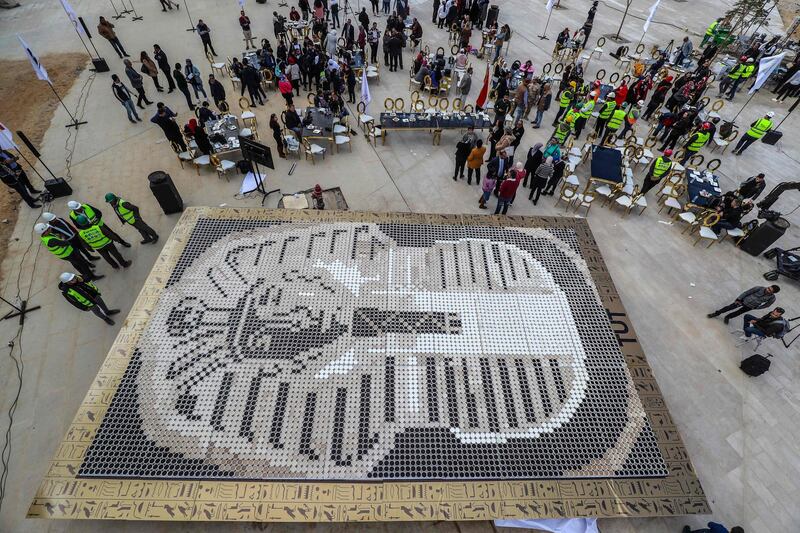 People gather around a depiction of the ancient Egyptian Pharaoh Tutankhamun's death mask made of 7260 cups of coffee, in front of the newly-built Grand Egyptian Museum (GEM) in Giza, on the southwestern outskirts of the capital Cairo.  AFP