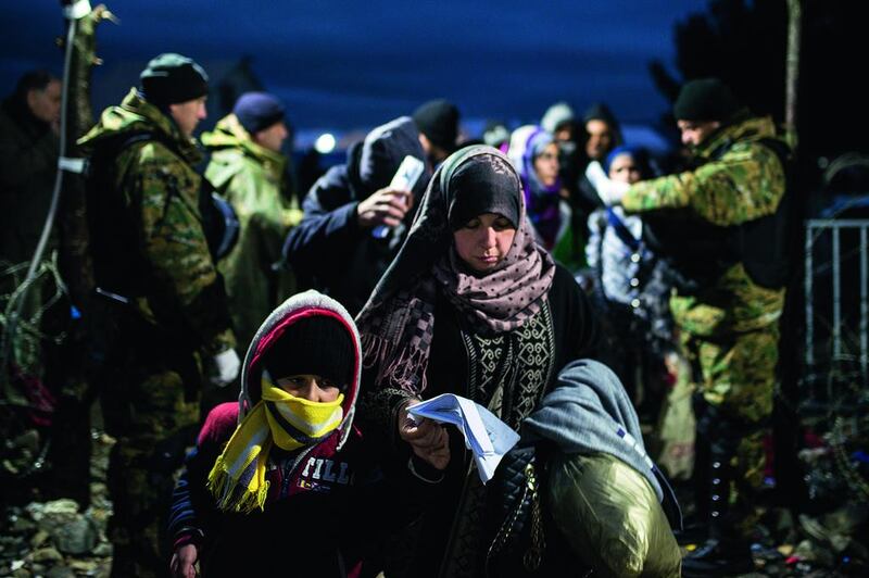 A woman and child walk past Macedonian police officers, as migrants and refugees cross the Greece-Macedonia border in November near Gevgelija. Over 200 migrants on November 26 tried to break through barbed wire fences to cross from Greece into Macedonia, which imposed new border restrictions. Robert Atanasovsi / AFP