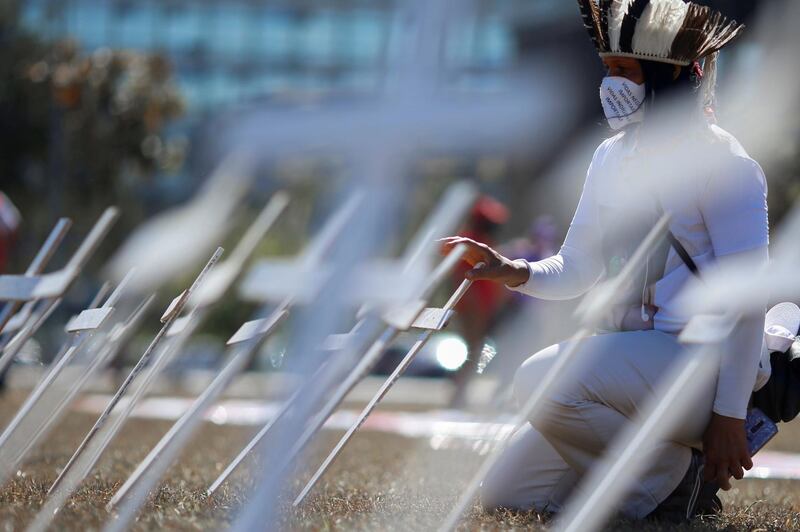 An activist kneels next to crosses symbolising the ones who died from the coronavirus in front of the National Congress during a protest against Brazil's President Jair Bolsonaro in Brasilia, Brazil. Reuters