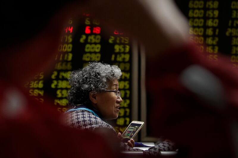 In this April 3, 2018 photo, a woman chats with her friends as they monitor stock prices at a brokerage house in Beijing. Shares were higher in Hong Kong and South Korea on Monday, April 30, 2018,  following the release of reassuring manufacturing data for China, though many Asian markets are closed for holidays. (AP Photo/Andy Wong)