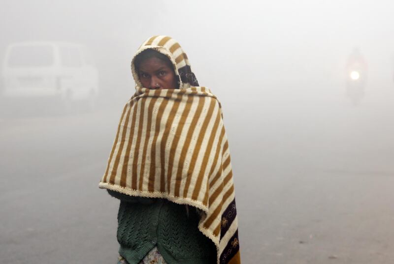 An Indian woman with a blanket wrapped around her walks along a road during a cold morning.  EPA