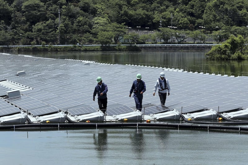 Workers walk past rows of solar panels at the 2.3-megawatt floating solar power station operated by Kyocera TCL Solar LLC, a joint venture between Kyocera Corp. and Century Tokyo Leasing Corp., on Sakasamaike Pond in Kasai, Hyogo Prefecture, Japan, on Sunday, May 24, 2015. The plant, with panels set up on a reservoir, is the world's largest floating solar plant, Kyoto-based Kyocera said in a statement Monday. Photographer: Buddhika Weerasinghe/Bloomberg