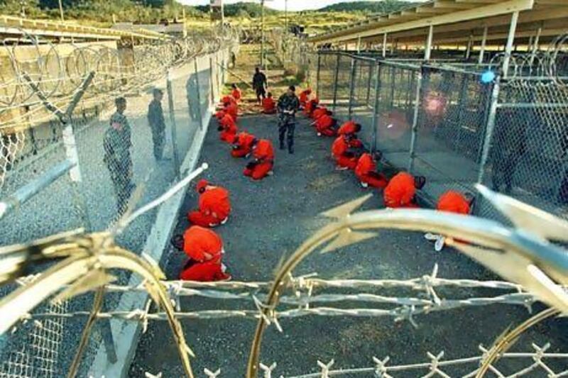 Detainees in orange jumpsuits sit in a holding area under the surveillance of US military police at Camp X-Ray at the US naval base, Guantanamo Bay, Cuba, during processing in 2002.