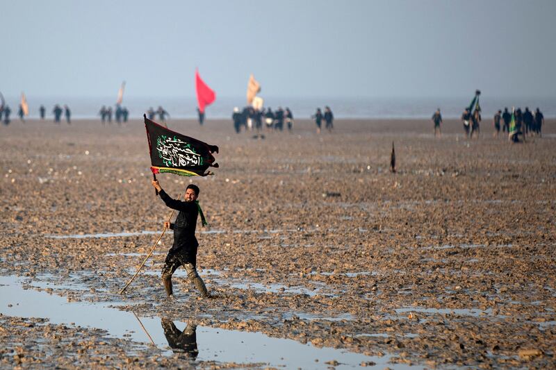 A Shiite Muslim pilgrim waves a flag as he walks in mud near the Gulf waters at the start of his march from Iraq's southern city of Al Faw towards Karbala.