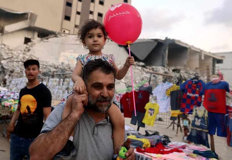 A Palestinian carries his child before the Eid Al Adha holiday, near the rubble of Al Shurouq tower in Gaza City's Al Rimal neighbourhood, which was hit by Israeli air strikes in May fighting.