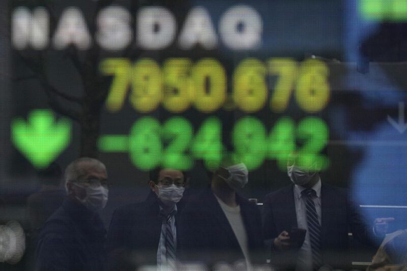 People wearing protective face masks, following an outbreak of the coronavirus, are reflected in a screen displaying NASDAQ movements outside a brokerage in Tokyo, Japan. Reuters