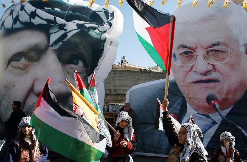 Palestinian school girls wearing the traditional chequerred keffiyeh headdress wave national flags and Fatah banners in front of huge portraits of late Palestinian leader Yasser Arafat (L) and his successor, current Palestinian Authority president Mahmud Abbas, during celebrations marking the 46th anniversary of the creation of their Fatah movement on January 3, 2011 in the West Bank city of Ramallah. The secular Fatah movement was founded by the iconic late Palestinian leader in the 1950s and formally launched its armed struggle against Israel on January 1, 1965. AFP PHOTO/ABBAS MOMANI / AFP PHOTO / ABBAS MOMANI