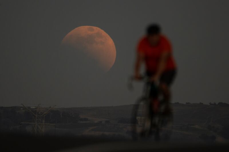 A lunar eclipse is seen behind a cyclist during the first Blood Moon of the year, in Irwindale, California. AP Photo