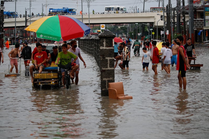People in the Philippines wade along a flooded road in Las Pinas city, south of the capital Manila, during a monsoon.