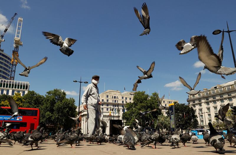 A man wearing a face mask feeds pigeons in front of Marble Arch, as the outbreak of the coronavirus disease (COVID-19) continues in London, Britain June 22, 2020. REUTERS/John Sibley