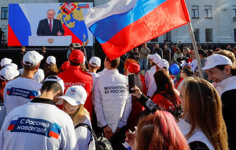 People gather near a screen showing Mr Putin during a broadcast of the ceremony. Reuters