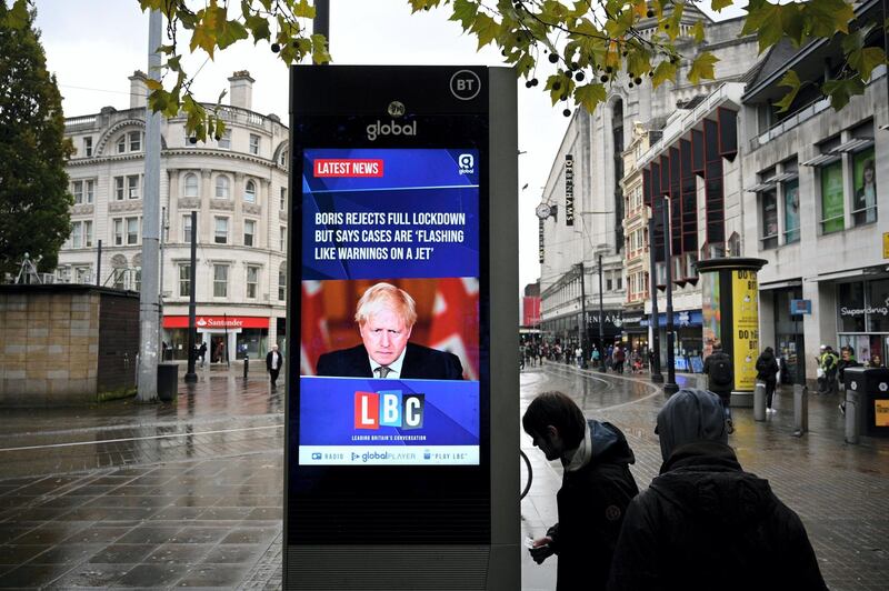 A news display features Britain's Prime Minister Boris Johnson as shoppers make their way along the streets of  Manchester, north west England on October 13, 2020, as the number of cases of the novel coronavirus COVID-19 continue to rise. - The British government faced renewed pressure on October 13, after indications it had ignored scientific advice three weeks ago for tougher restrictions to cut rising coronavirus infections. (Photo by Oli SCARFF / AFP)