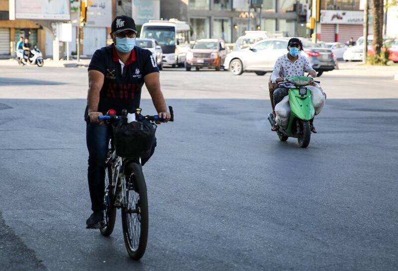 A mask-clad man rides a bicycle while another rides a scooter along a street in the central Karrada district of Iraq's capital Baghdad.  AFP