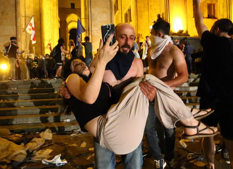 An opposition demonstrator carries a woman during a protest at the Georgian Parliament to call for the resignation of the speaker of the Georgian Parliament in Tbilisi, Georgia, Friday, June 21, 2019. Police have fired a volley of tear gas at a massive throng of protesters outside the Georgian national parliament, who are trying to storm the building and are demanding the government's resignation.(AP Photo/Zurab Tsertsvadze)