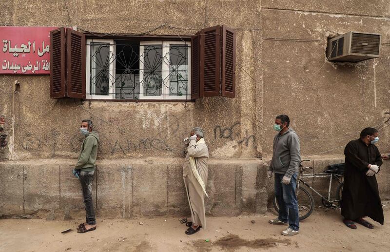 Egyptian men wearing masks wait outside a centre of non-governmental organisation Egyptian Food Bank to receive cartons with foodstuff in the Egyptian capital Cairo.  AFP