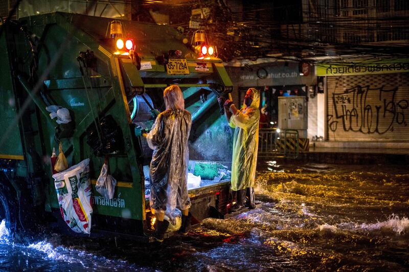 Waste disposal workers wear ponchos as they ride down a flooded street after heavy rain in Bangkok. AFP