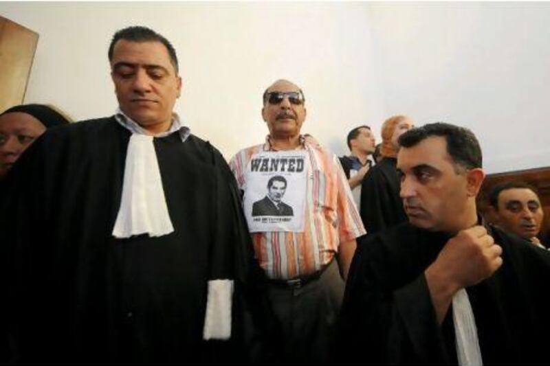 A man holds a poster reading 'Wanted for Dictatorship' and showing deposed Tunisian president Zine el Abidine ben Ali as he stands outside the court house yesterday during the opening of the trial of Ben Ali and his wife Leila in Tunis. Fethi Belaid / AFP Photo