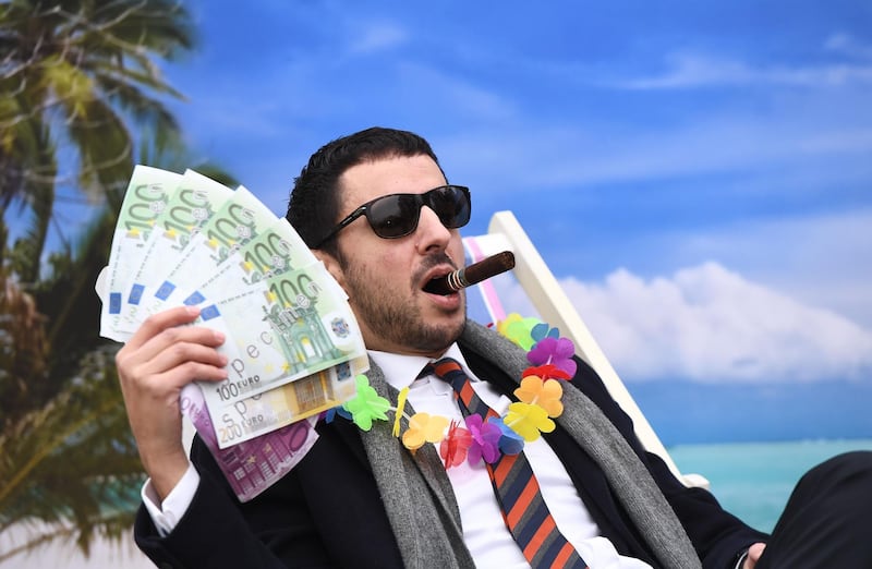 An Oxfam activist stages a satirical street-play mimicking a wealthy person hidding his money in a tax haven, on December 5, 2017 near the European institutions in Brussels, within a meeting of European Union ministers over a credible blacklist of non-EU tax havens. 
The EU has struggled for over a year to finalise the blacklist, with smaller, low-tax EU nations such as Ireland, Malta and Luxembourg worried about scaring off multinationals. / AFP PHOTO / EMMANUEL DUNAND