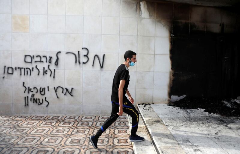 A Palestinian man walks past a Hebrew slogan reading "a siege for Arabs, not for Jews! the Land of Israel for the People of Israel" after a mosque section was set on fire, in Al-Bireh in the Israeli-occupied West Bank July 27, 2020. REUTERS/Mohamad Torokman