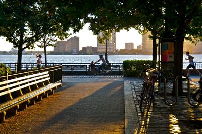 "New York City, USA - August 18, 2012: A bicyclist  and runners are seen passing by a woman sitting along the Battery Park City Promenade during a summer sunset over the Hudson River, Lower Manhattan." Getty Images