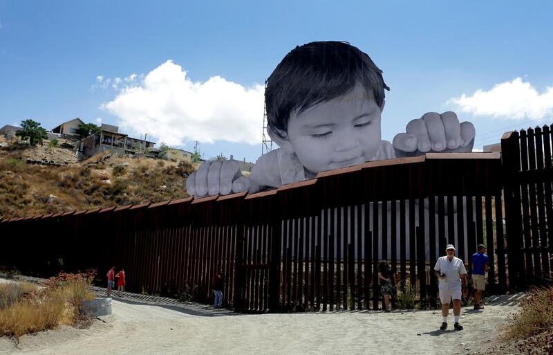epaselect epa06197366 A 70 feet (about 21 meter) tall art installation created by French artist JR rises above and appears to peek over the border wall that bisects Tecate, Mexico and Tecate, California, USA, 10 September 2017. The art piece utilizes a large black and white photograph in a public place in the same fashion as graffiti art.  EPA-EFE/PAUL BUCK