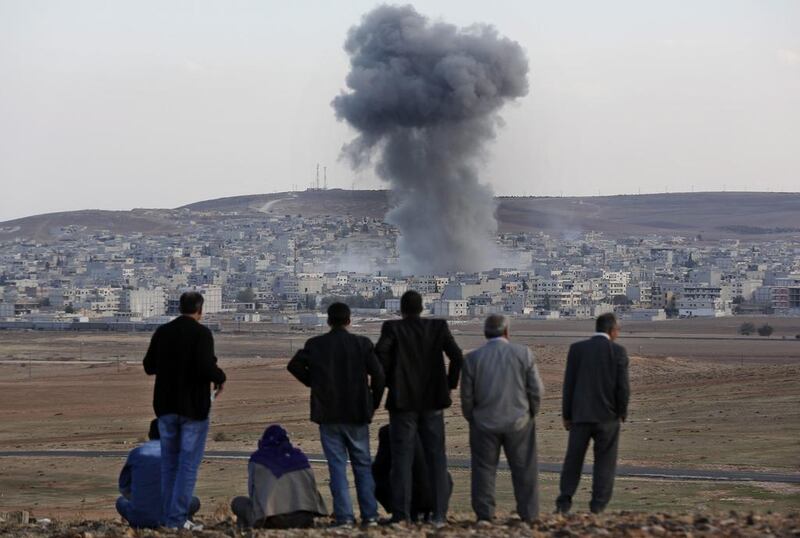 Smoke from an explosion rises over the Syrian city of Kobani as people on the Turkish side of the border look on. Sedat Suna / EPA
