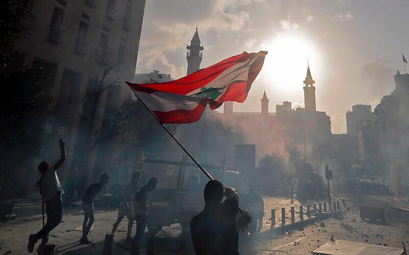 A Lebanese protester waves the national flag during clashes with security forces in downtown Beirut on August 8, 2020, following a demonstration against a political leadership they blame for a monster explosion that killed more than 150 people and disfigured the capital Beirut.  / AFP / JOSEPH EID
