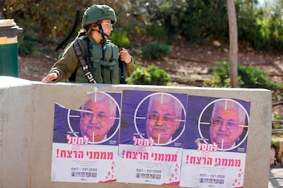 An Israeli soldier stands next to posters bearing a picture of Palestinian Authority President Mahmud Abbas with a slogan reading in Hebrew: "Eliminate the people sponsoring murder", near the Israeli settlement of Migron in the occupied West Bank on December 11, 2018. Seven people were wounded in a drive-by shooting by Palestinian gunmen at a bus stop near the Ofra settlement in the occupied West Bank late on December 9, with doctors forced to prematurely deliver the baby of one of the wounded, Israeli officials said. / AFP / Menahem KAHANA
