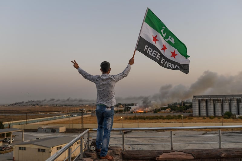 A man waves a Syrian opposition flag reading "Free Syria" in Akcakale as smoke rises in the background from the Syrian border city of Tal Abyad seized by Turkish forces and their proxies. AFP