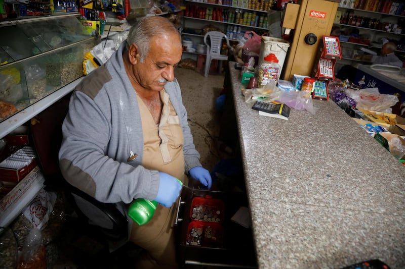 A Palestinian man sprays disinfectants to sanitise coins at his shop in Jordan Valley in the Israeli-occupied West Bank. Reuters