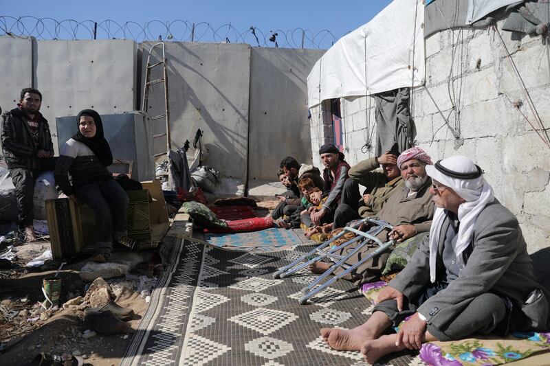 An internally displaced Syrian family sit together outside a tent near the wall in Atmeh IDP camp. Reuters