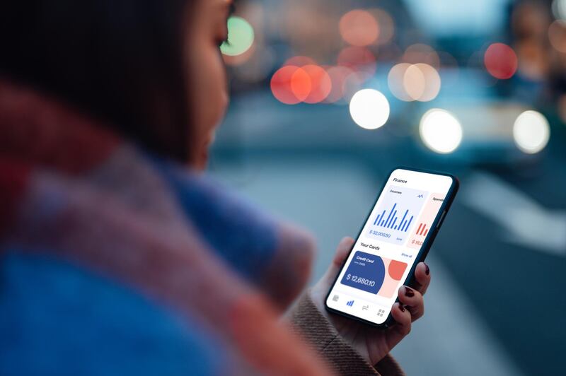 Over the should view of young Asian woman checking financial data of her credit card account on smartphone. Making a budget plan for her expense. Business on the go concept.