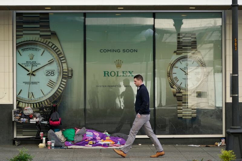 A person sleeps beside a shopping cart as a pedestrian walks past, in downtown Seattle, US. AP