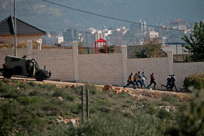 Palestinian protesters run away as an Israeli security vehicle chases after them amid clashes following a demonstration against the expansion of settlements in the Israeli-occupied West Bank.  AFP
