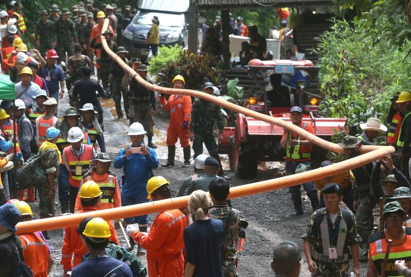 Rescuers carry water piping at the entrance to a cave complex where the 12 boys and their football coach were trapped inside when heavy rains flooded the cave, in Mae Sai, Chiang Rai province, in northern Thailand. Sakchai Lalit / AP Photo