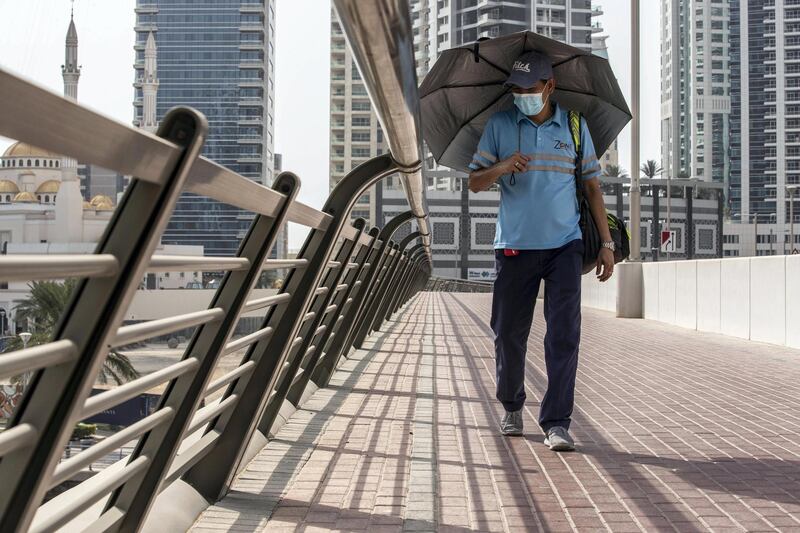DUBAI, UNITED ARAB EMIRATES. 18 JULY 2020. A man shades himself from the sun while walking along a footpath crossing a bridge in the Dubai marina. Hot and hazy weather in Dubai and the UAE as the full force of summer weather hits during the COVID-19 pandemic with residents unable to easily travel due to the preventative measures put in place. (Photo: Antonie Robertson/The National) Journalist: STANDALONE Section: National.