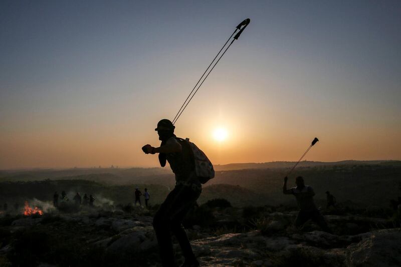 Palestinian protesters use slingshots to hurl stones during clashes with Israeli security forces in the village of Ras Karkar, west of Ramallah, in the occupied West Bank. Abbas Momani/AFP