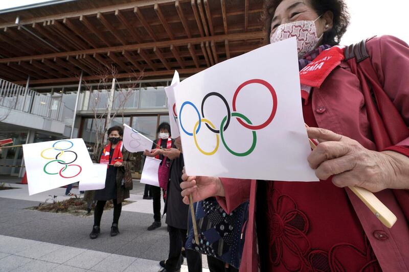 Local residents carry handmade flags featuring Olympic Rings at the torch relay route of the first section of the Fukushima Torch Relay in Naraha, Fukushima prefecture, northeastern Japan, Thursday, March 25, 2021. The torch relay for the postponed Tokyo Olympics began its 121-day journey across Japan on Thursday and is headed toward the opening ceremony in Tokyo on July 23. (AP Photo/Eugene Hoshiko)