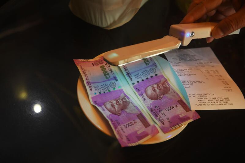 A waiter uses ultraviolet light to disinfect notes at a restaurant in Mumbai. AFP